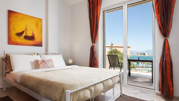 A bedroom with a bed, a painting, and a view of the sea through a sliding door.
