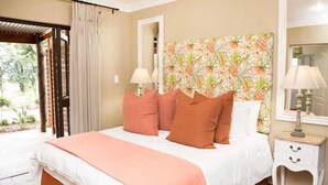 Un dormitorio con cama, almohadas, mesita de noche, lámpara, espejo y ventana con cortinas.