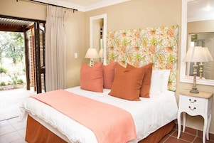 Un dormitorio con cama, almohadas, mesita de noche, lámpara, espejo y ventana con cortinas.