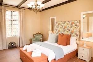 Un dormitorio con cama, una silla, una mesita de noche, un ventilador y una ventana con cortinas.