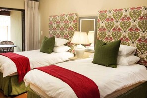 A hotel room with two beds, each with white linens and green pillows, a red throw blanket, a nightstand with a lamp, and a mirror on the wall. - Remhoogte Mountain Lodge (Skeerpoort)