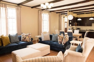 Una sala de estar con sofá, reposapiés, sillas y una zona de cocina con armarios y una mesa de comedor.