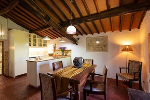 A rustic kitchen with wooden beams, a dining area with a wooden table and chairs, and a kitchen island with a sink and counter.