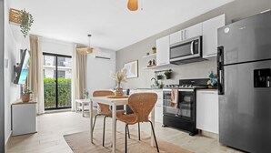 A modern kitchen with white cabinets, stainless steel appliances, and a dining area with wicker chairs and a table. - NOK Cozy 1BR Retreat With Pool Near Punta Cana Beaches (Punta Cana)