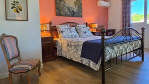 Un dormitorio con cama, una silla, un cuadro, aire acondicionado y una ventana.