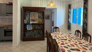 Comedor con mesa, sillas, mantel estampado, lámpara colgante y aparador decorativo con cuadros enmarcados.