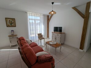 A living room with a sofa, a TV on a cabinet, a chair, a table, and a window with curtains. - Peaceful cottage between fields and forests - 6 guests (Gidy)