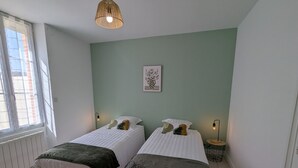 Ein Zimmer mit zwei Betten, einem Fenster mit Jalousien, einer Pendelleuchte und einem gerahmten Bild an der Wand.