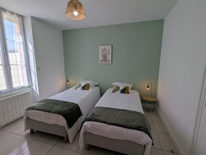 A room with two beds, a window with blinds, a hanging light fixture, and a framed picture on the wall. - Peaceful cottage between fields and forests - 6 guests (Gidy)