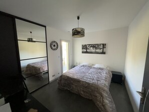 Een slaapkamer met een bed, een spiegel, een klok, een deur en een plafondlamp.