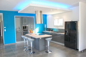 Une cuisine moderne dotée d’un îlot central, d’appareils électroménagers en acier inoxydable et d’un mur d’accent bleu.