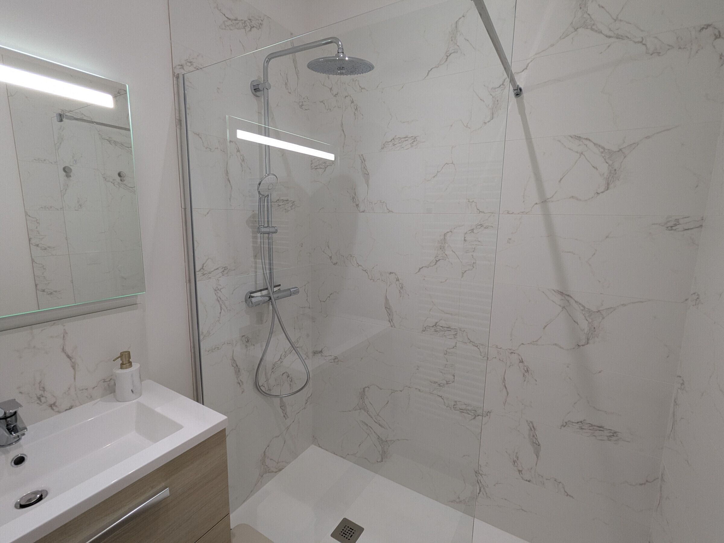 Une salle de bain moderne avec une douche, un lavabo et un miroir.