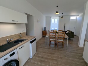 Une cuisine moderne équipée d’un lave-vaisselle, d’un lave-linge encastré, d’un coin repas avec des chaises en bois et d’un salon avec un canapé.