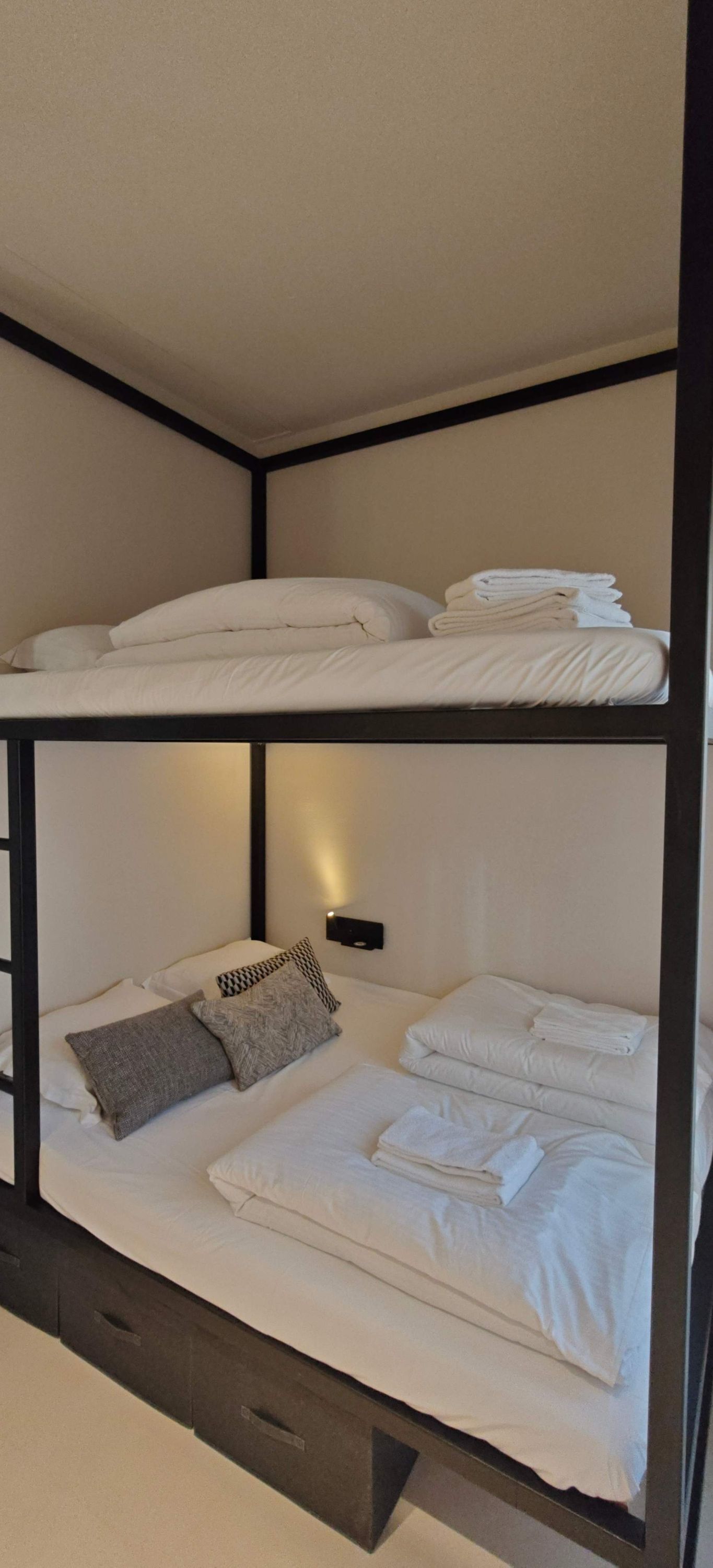 Un lit superposé avec une literie blanche et un luminaire fixé au mur.