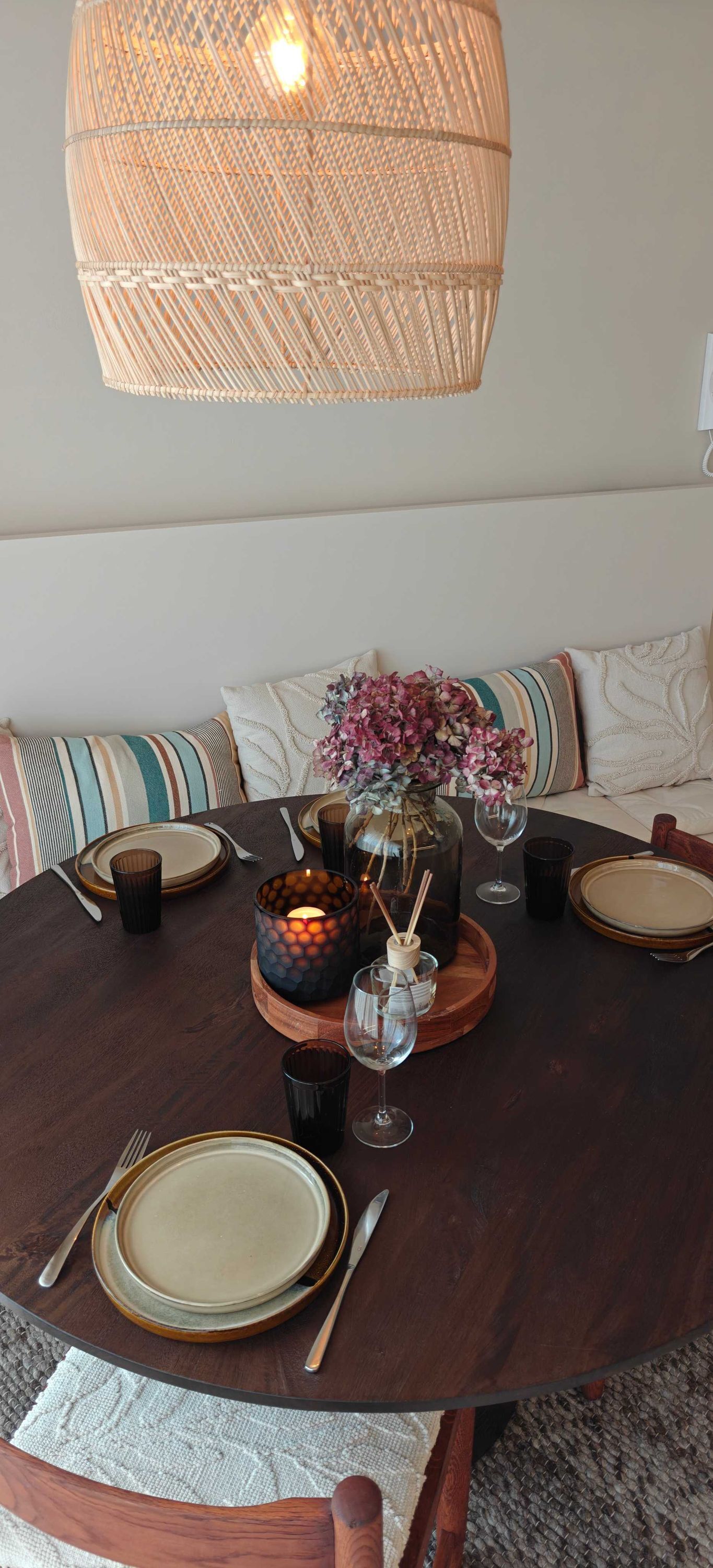 A round dining table with a woven light fixture above, surrounded by cushioned seating.