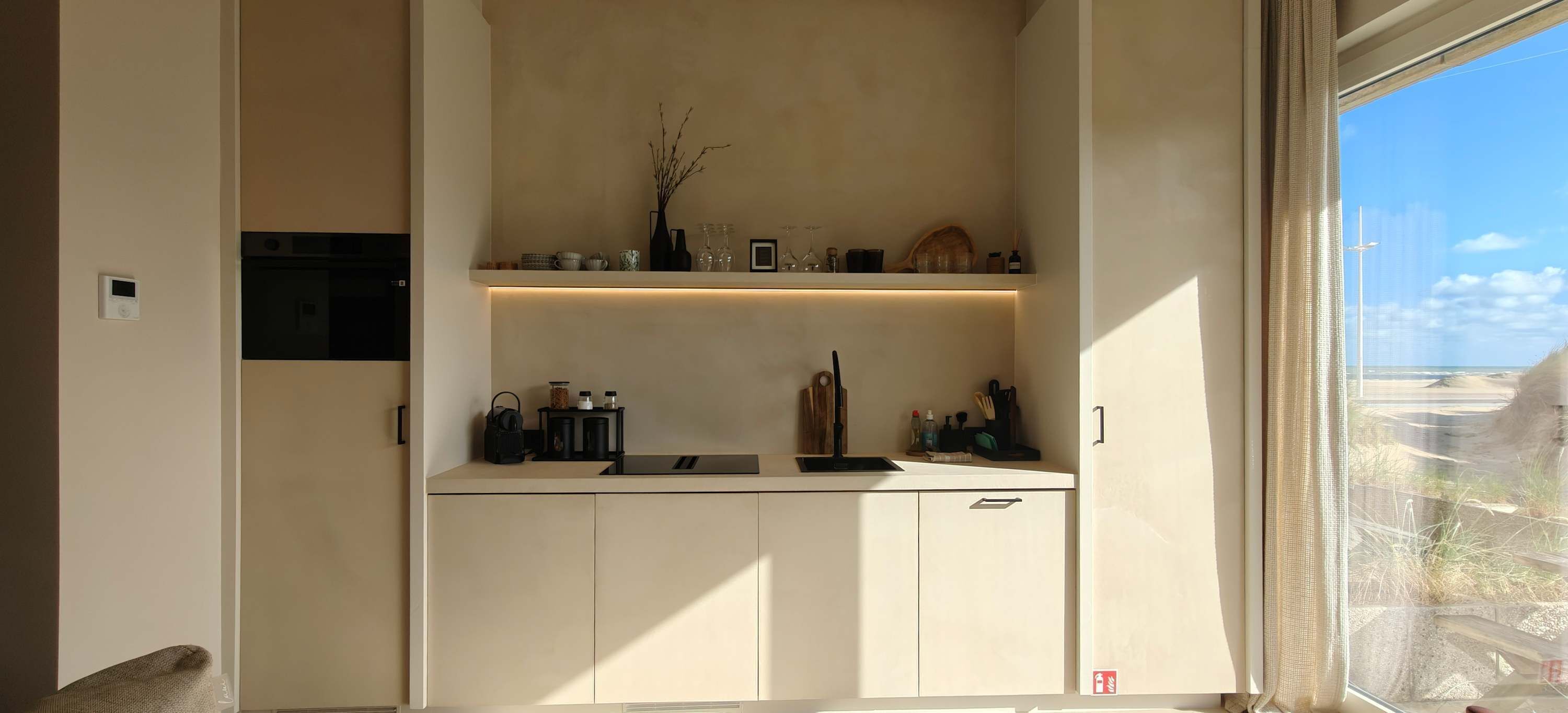 A modern kitchen with built-in appliances, a window with a view, and a shelf with decorative items.