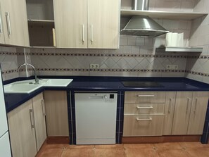 Una cocina con armarios de madera clara, lavavajillas, fregadero y salpicadero de azulejos.
