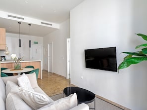 A modern living room with a sofa, a black chair, a TV mounted on the wall, and a large green plant. - Apartment in the heart of Málaga (Málaga)