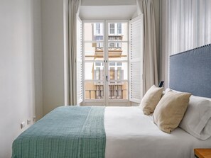 A bedroom with a bed, pillows, a window with shutters, and a view of a balcony. - Apartment in the heart of Málaga (Málaga)