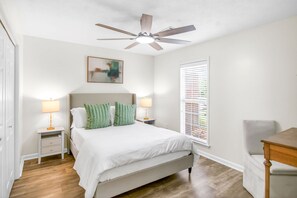 A bedroom with a bed, two bedside tables with lamps, a ceiling fan, a window with blinds, and a chair. - Spacious East Montgomery Home With Patio (Montgomery)