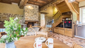 Un interno rustico con camino in pietra, tavolo da pranzo in legno e cucina con frigorifero in acciaio inossidabile.