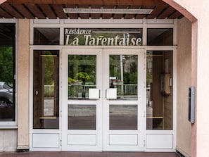 Ein Gebäudeeingang mit Doppeltüren, eine Beschilderung mit der Aufschrift 'Résidence La Tarentaise' und ein kleines Fenster mit Blick auf Grünflächen.