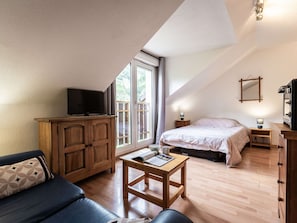 Ein gemütliches Zimmer mit einem Bett, einem Fernseher auf einer Holzkommode, einem kleinen Tisch und einem Fenster mit Blick.