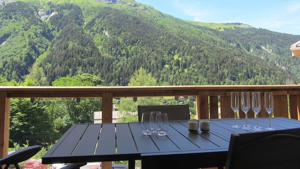 A wooden deck with a table and chairs, overlooking a mountainous landscape. - Spacious apartment mountain view - 6 guests (Les Contamines-Montjoie)