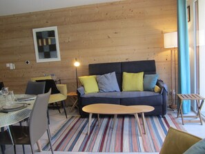 Ein gemütliches Zimmer mit einer Couch, Sesseln, einem Esstisch und einer Lampe.