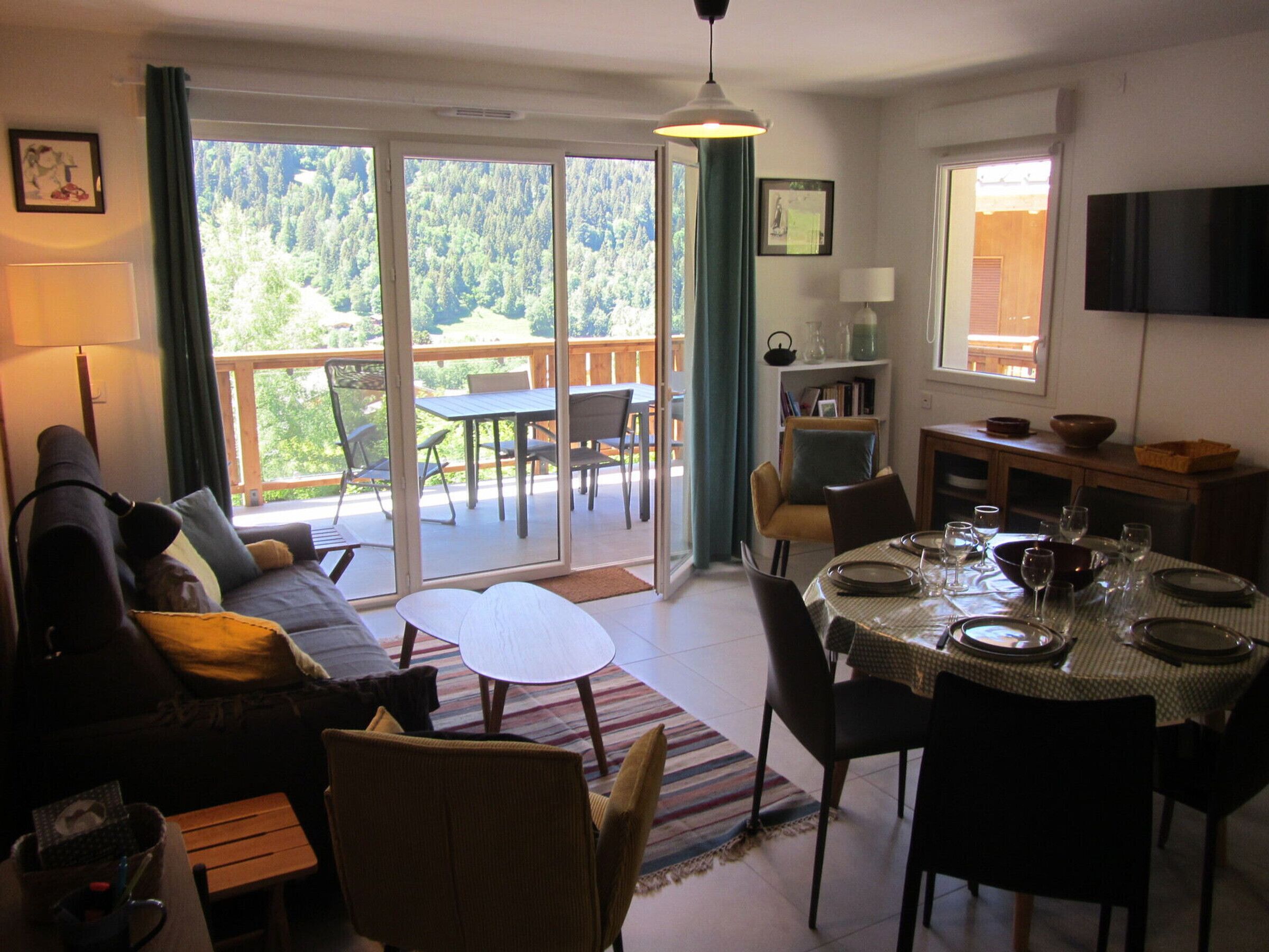 A living room with a sofa, a dining table set for four, and a balcony with a table and chairs.