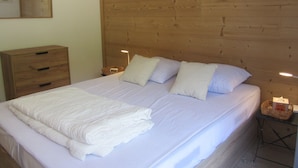 A neatly made bed with pillows, a wooden headboard, a nightstand with a lamp, and a wooden dresser. - Spacious apartment mountain view - 6 guests (Les Contamines-Montjoie)