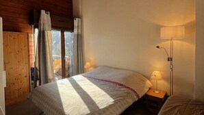 A bedroom with a bed, a nightstand, a lamp, and a window with curtains. - Comfortable duplex - 6 guests (Châtel)