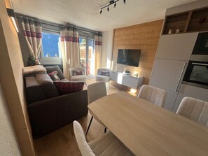 A compact living space with a sofa, dining table, chairs, a TV, and a kitchen area.