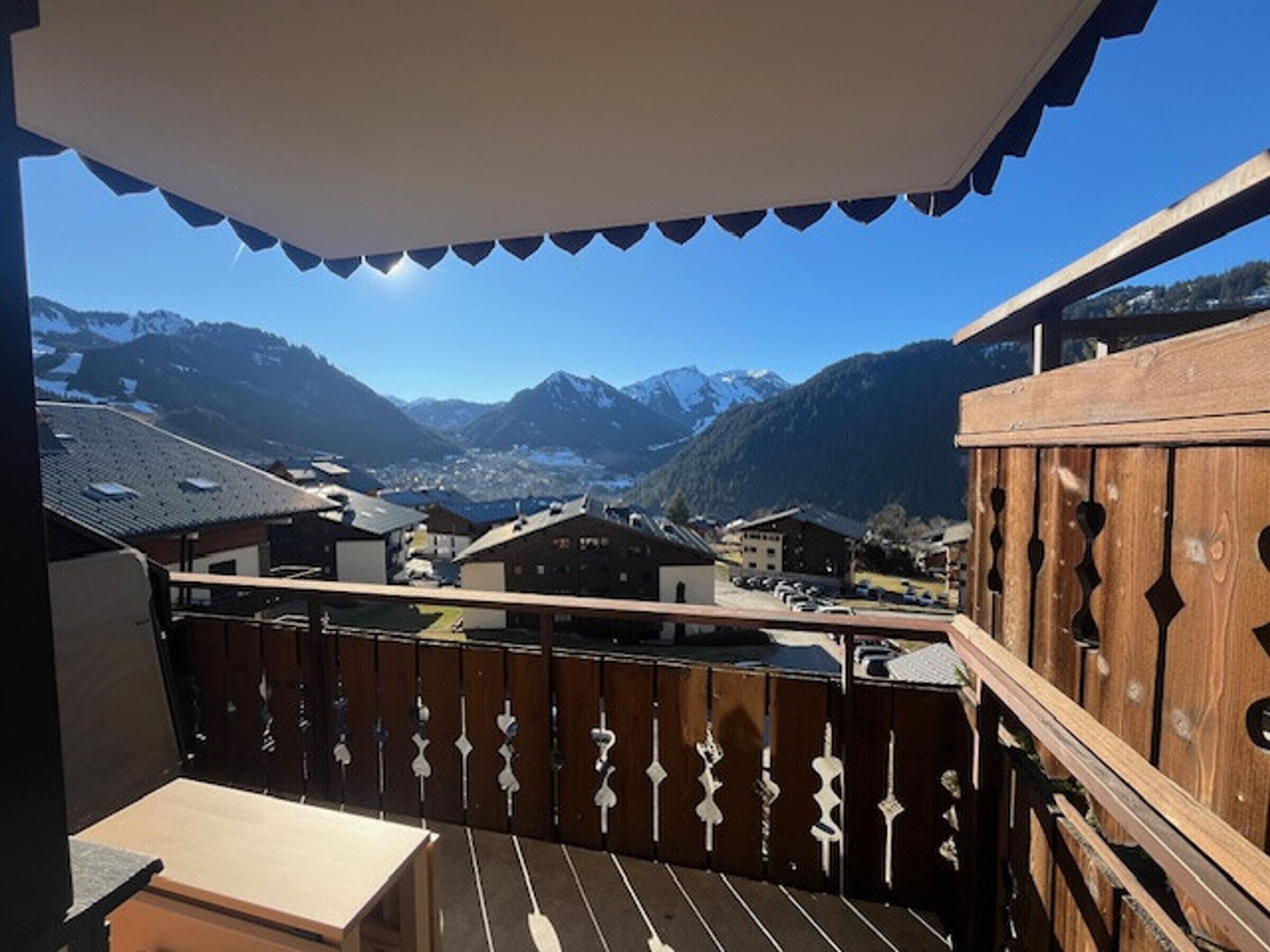 A balcony with a view of a mountain village, wooden railings, and a clear sky.