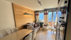 A cozy living area with a wooden wall, a sofa, a dining table with chairs, and a kitchen area with a refrigerator. - Comfortable duplex - 6 guests (Châtel)