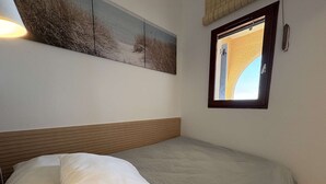 Een slaapkamer met een bed, kussens, een hoofdbord, een raam en een kunstwerk aan de muur.