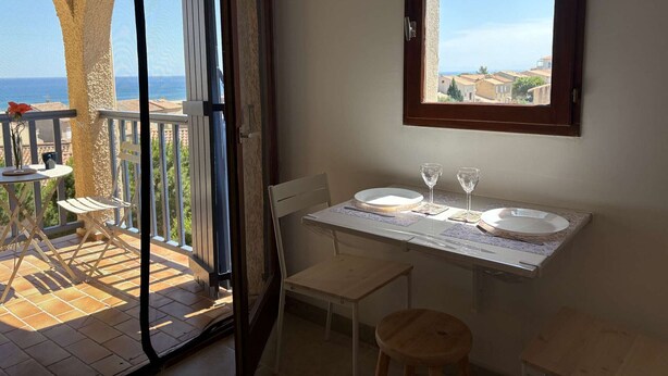 Een balkon met een tafel gedekt voor twee personen, een stoel en uitzicht op zee.