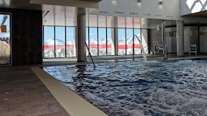 Una piscina interior con vistas a montañas nevadas, amplias ventanas y techo de madera.