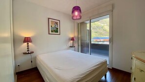 Un dormitorio con una cama, dos lámparas de noche, un cuadro y un ventanal corredero que da a un balcón.