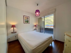 Ein Schlafzimmer mit einem Bett, zwei Nachttischlampen, einem Gemälde und einer Schiebetür, die auf einen Balkon führt.
