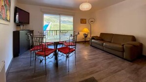 Una sala de estar con una mesa de comedor, sillas, un sofá, un televisor y un balcón con vistas.