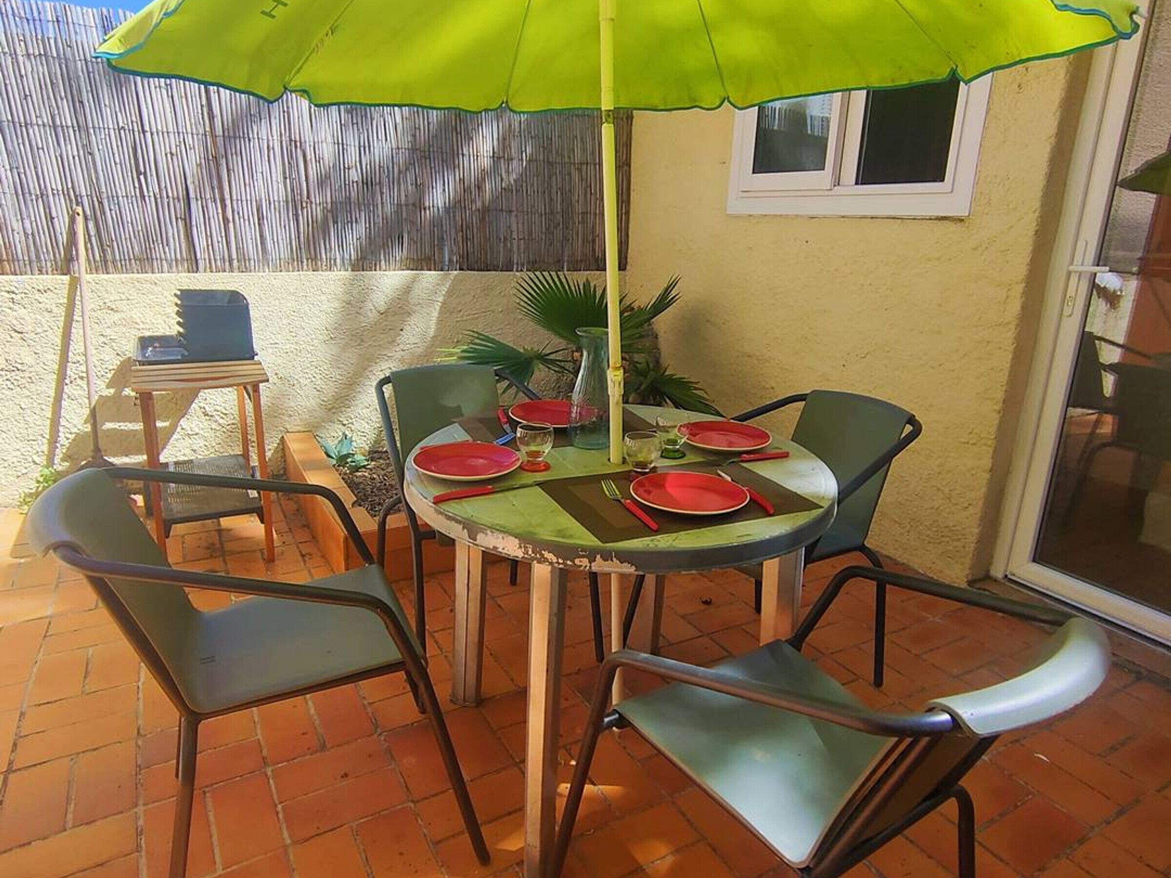 A patio with a table set for four, surrounded by chairs, under a green umbrella.