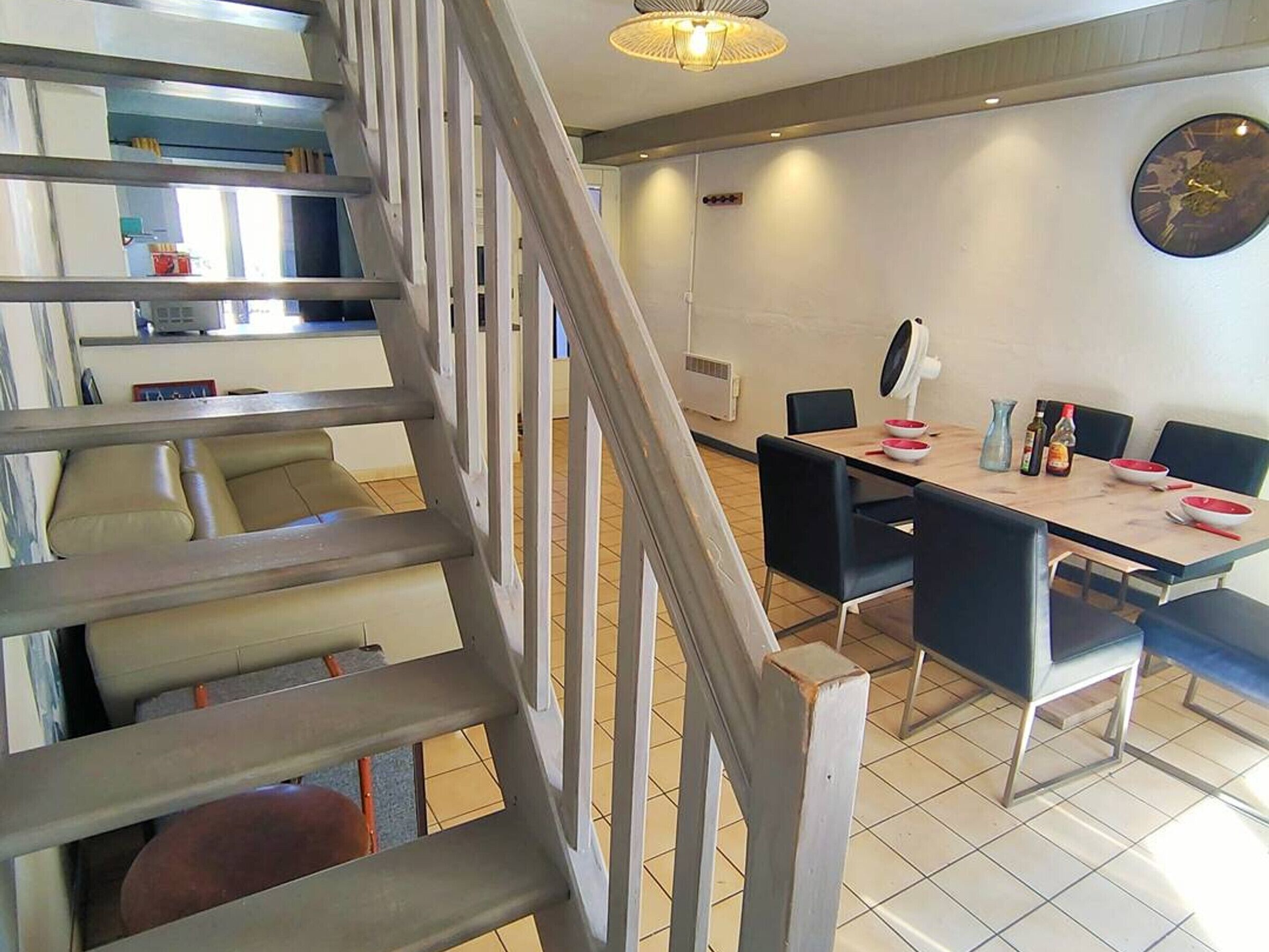 Een modern interieur met een trap, een eetgedeelte en een klok aan de muur.