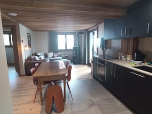 Eine moderne Küche mit dunklen Schränken, einem Holztisch und einem Sofa im angrenzenden Wohnbereich.