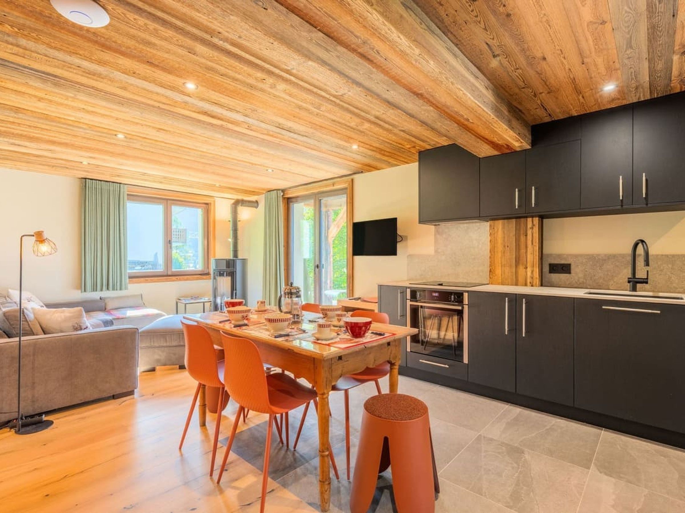 A modern kitchen with dark cabinets, a wooden dining table, and a built-in oven.