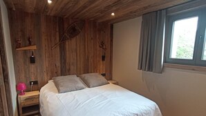 A bedroom with a wooden ceiling, a bed with white bedding, a nightstand with a lamp, and a window with curtains. - Spacious apartment near center - 6 guests (Châtel)