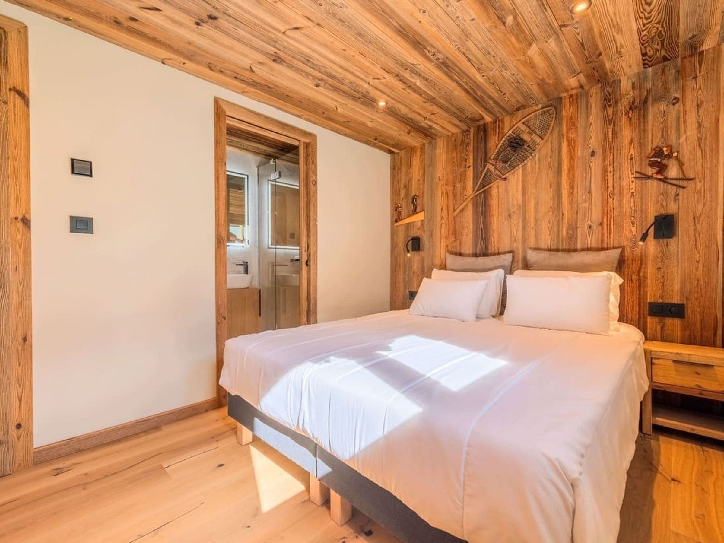 A bedroom with a wooden ceiling, a bed with white bedding, a wooden headboard, and a nightstand.