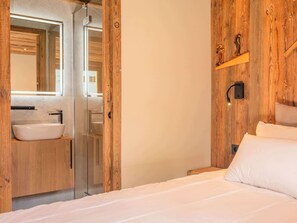 Ein Schlafzimmer mit Holzwand, einem Bett, einem Nachttisch, einem Schminktisch, einem Spiegel und einem Badezimmer mit Waschbecken und Dusche.
