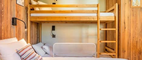 A bunk bed room with a wooden ceiling, a ladder, and a bed with pillows.