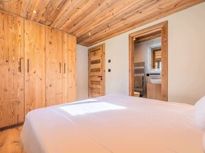 Une chambre avec un plafond en bois, un lit, une armoire en bois et une salle de bain avec un miroir et un lavabo.